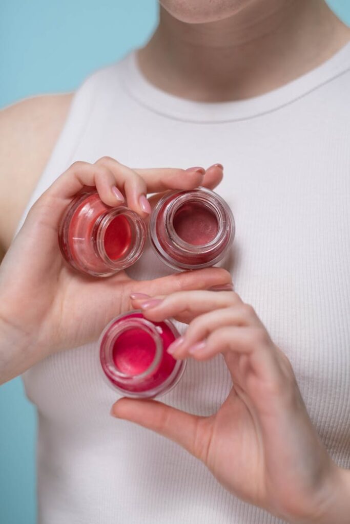 Close-up of a woman presenting vibrant makeup pots against a pastel background, showcasing modern beauty aesthetics.
